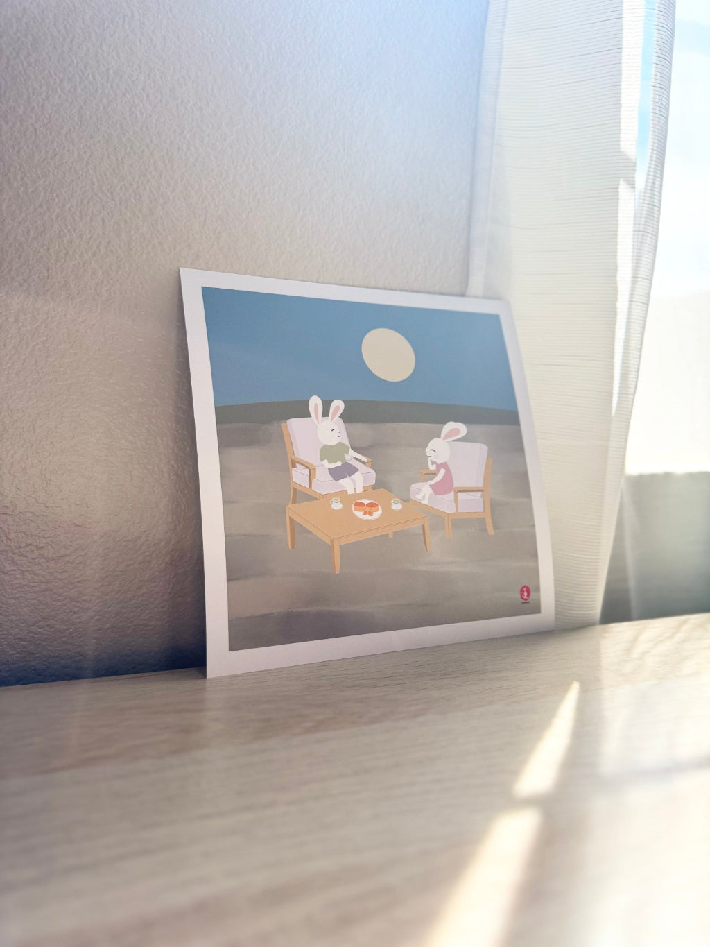 Printed artwork of two jade rabbits sitting at a table under a moonlit sky.