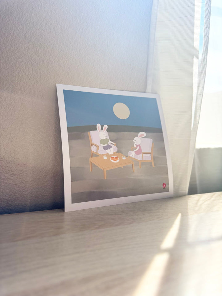 Printed artwork of two jade rabbits sitting at a table under a moonlit sky.