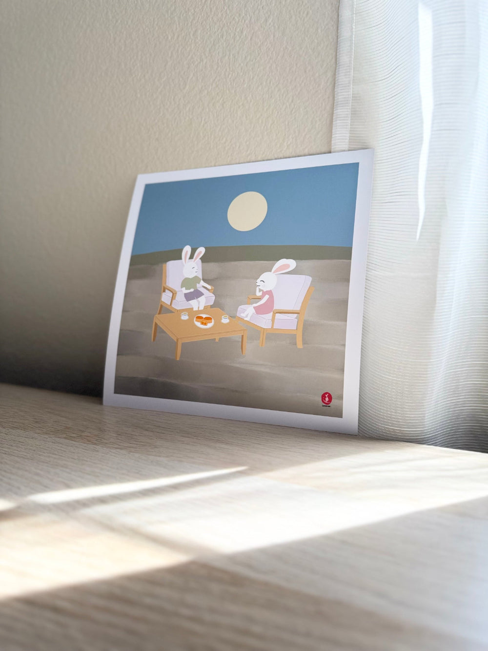Printed artwork of two jade rabbits sitting at a table under a moonlit sky.