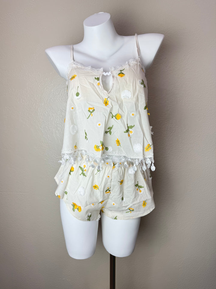 A cream-colored two-piece camisole set with a yellow and white floral print, displayed on a white mannequin torso against a neutral beige wall.