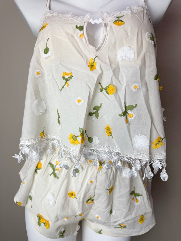 A cream-colored two-piece camisole set with yellow and white floral embroidery, displayed on a white mannequin torso. The set includes a sleeveless top with a keyhole cutout and ruffled trim, and matching shorts.