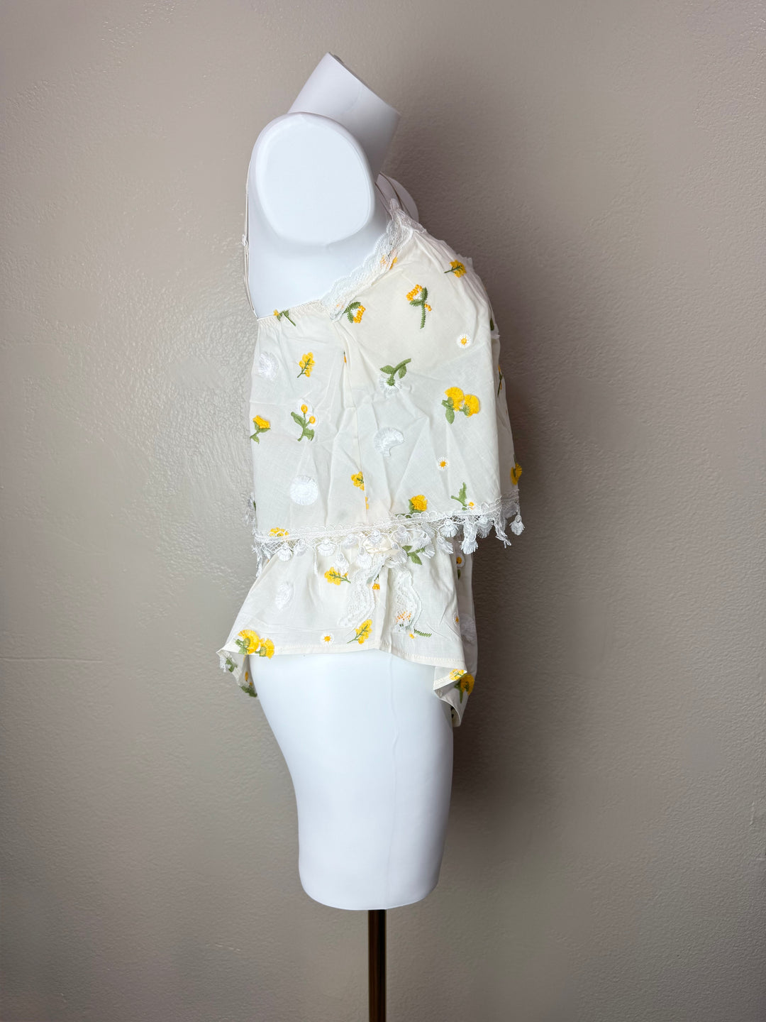 A white short-sleeve camisole set with a yellow and green floral print, displayed on a white mannequin torso against a plain beige wall.