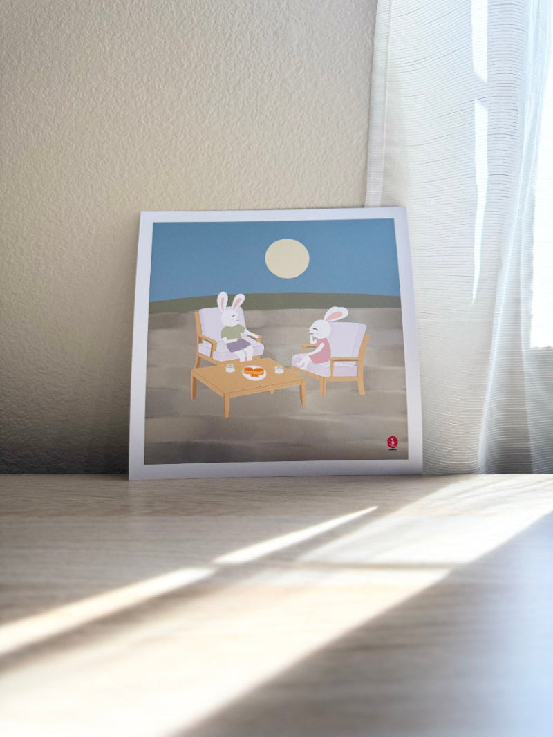 Printed artwork of two jade rabbits sitting at a table under a moonlit sky.