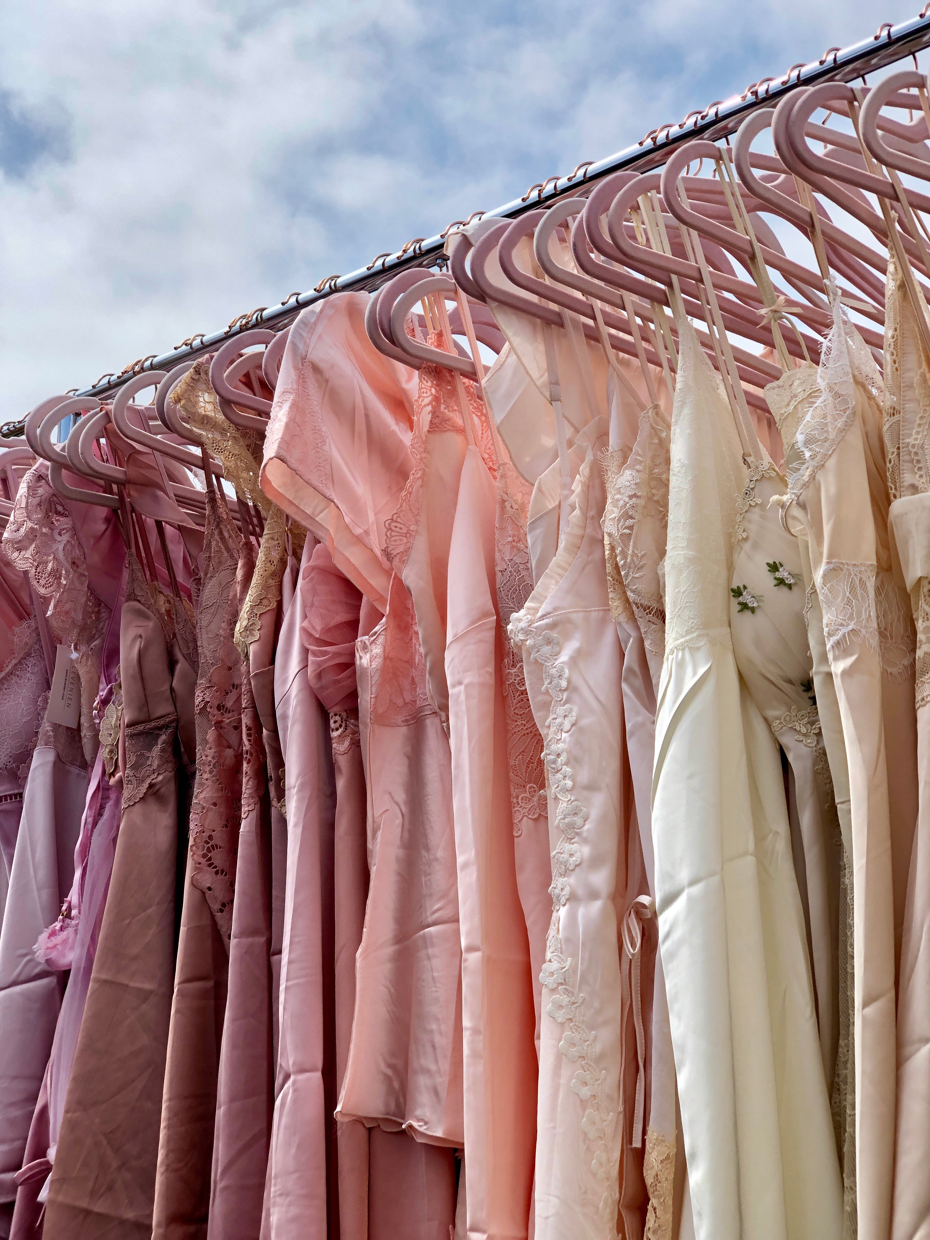 Row of pink and beige dresses hanging on a rack against a blue sky.
