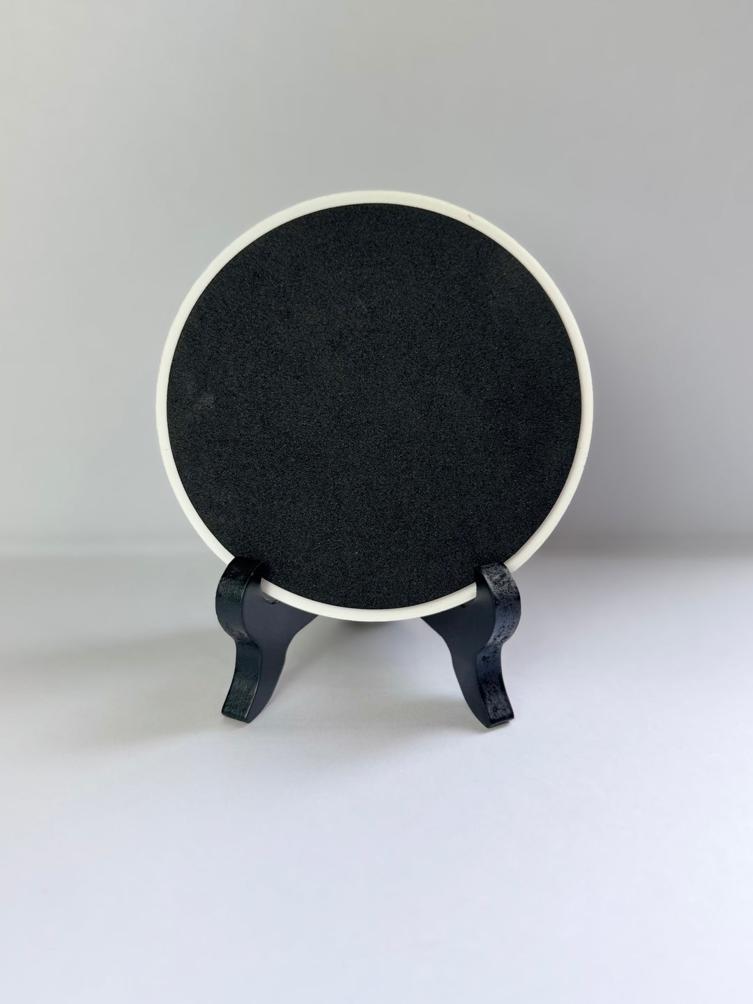 Back side of ceramic coaster placing on a stand against a gray background