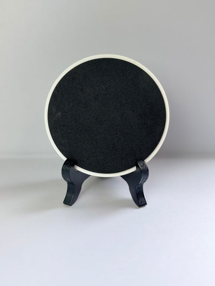 Back side of ceramic coaster placing on a stand against a gray background